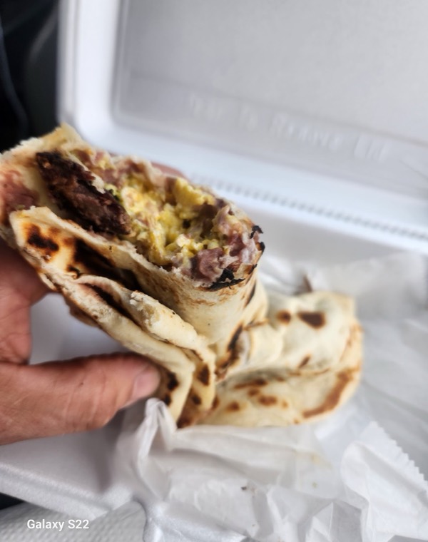 A folded baleada held open showing beans, egg and meat inside