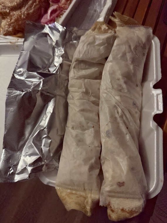 Two wrapped burritos in a to-go container next to foil