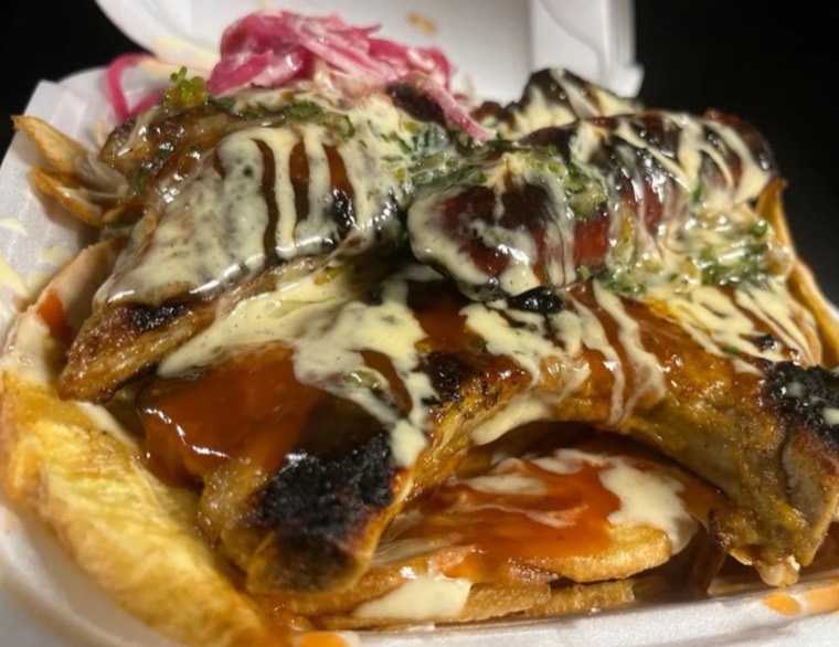 Pork chop over tajadas, dressed with crema and sauce, topped with pickled onion