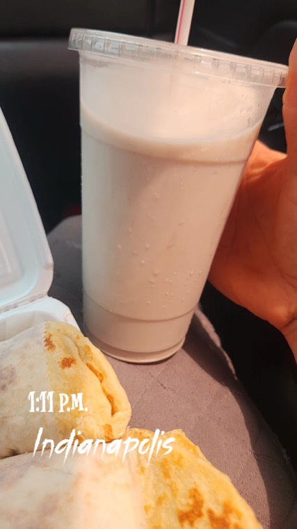 A tall cup of horchata next to a box of baleadas, photographed in a car