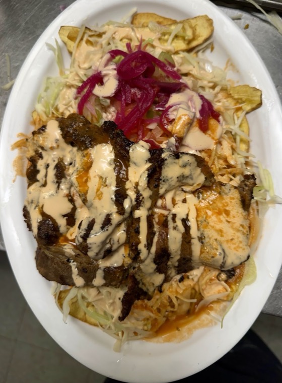 A large plate of grilled beef and chicken over tajadas with cabbage and pickled onion