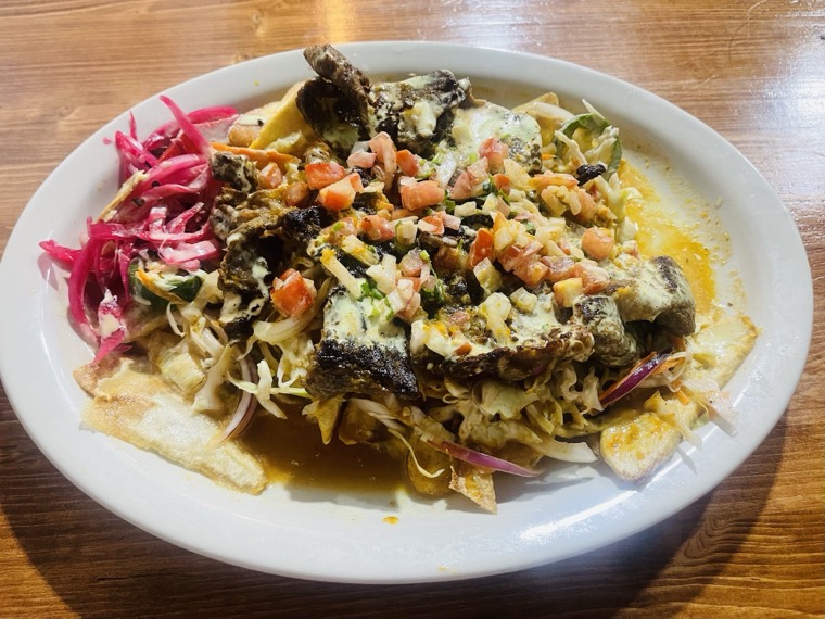 An oval plate of tajadas topped with meat, pico de gallo, cheese and pickled onion