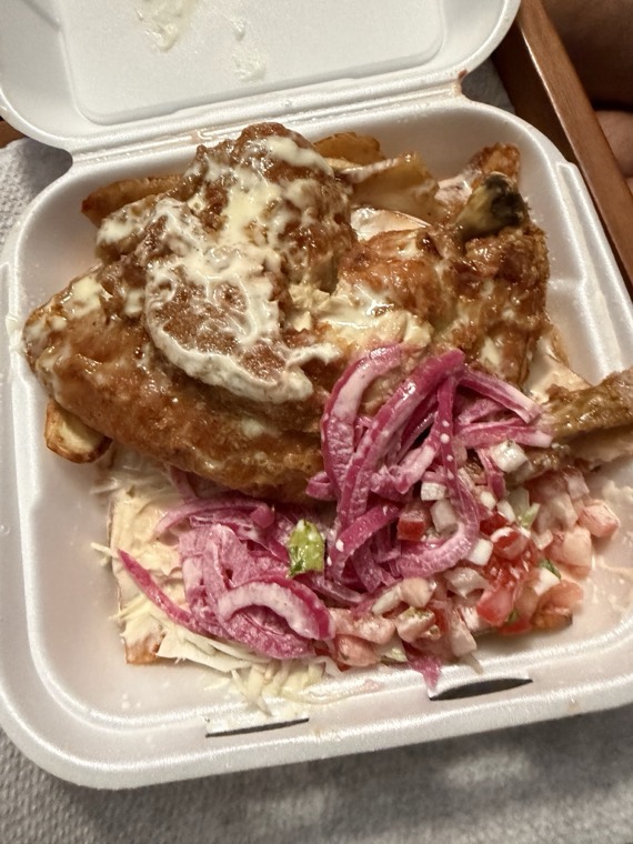 A to-go box of chicken over tajadas with shredded cheese and pickled onion