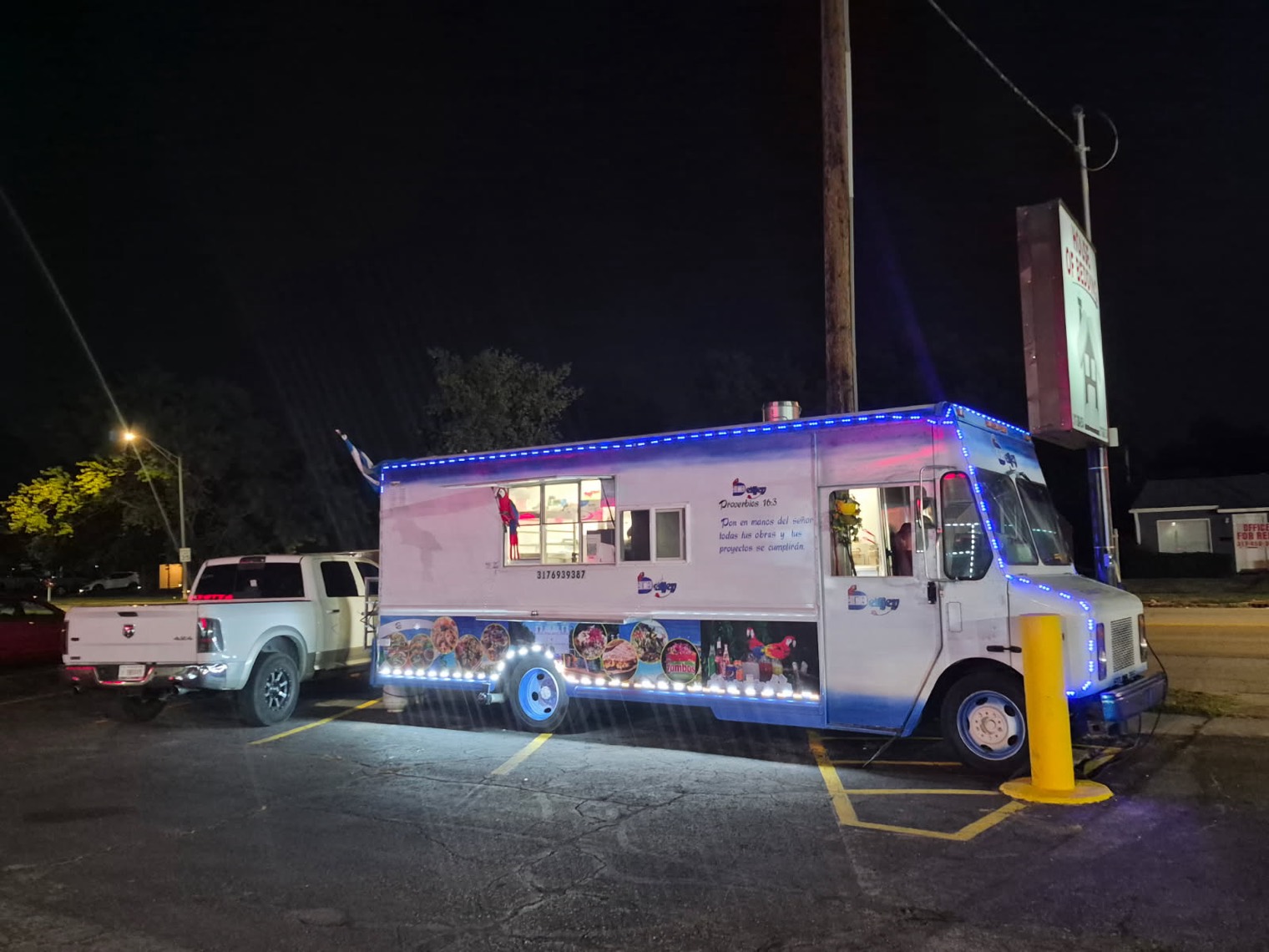 The DeliJey food truck lit up at night, blue and white with its lights on, parked on Commercial Drive